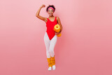 Full length view of strong african woman in aerobics form. Laughing black girl with fitness mat showing muscles.