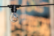 A Single Bare Outdoor Light Bulb Hangs From Its Socket On A Black Electrical Wire