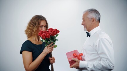 Wall Mural - A loving elderly husband presents a gift and roses to a mature smiling woman.