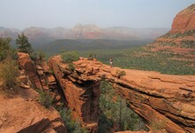 An Unrecognizable Person On Devil's Bridge, The Natural Arch Formation, With Red Rock Mountains In The Background Located In Sedona, Arizona