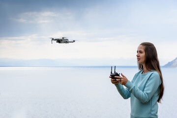 Wall Mural - Beautiful young woman having fun with a mini drone outdoors. The girl stands against water background