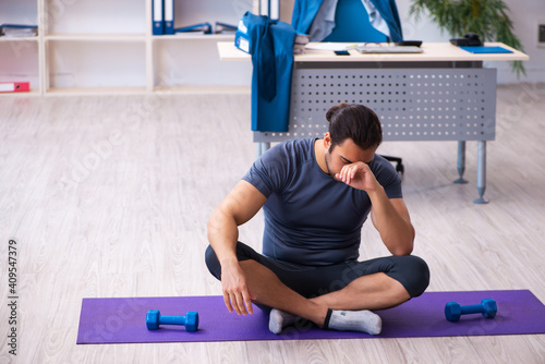 Young handsome employee doing sport exercises in the office