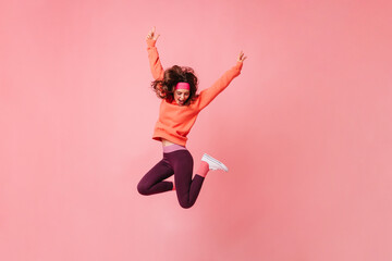 Wall Mural - Lovely brunette girl in pink sports headband and tracksuit jumps on isolated pink background