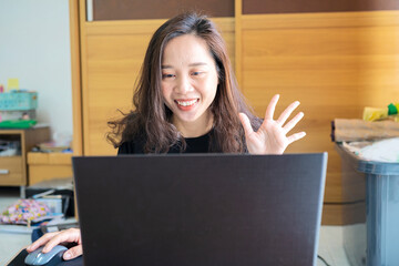 Girl making a video call online on the internet. Smiling Asian businesswoman in headset waving hand, using laptop