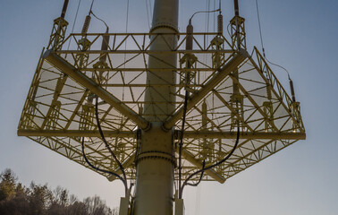 Low angle view of grid support of large electrical tower with sun shining from behind tower.