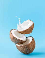 cracked coconut with splashes of milk on blue background