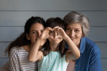 head shot portrait little girl with young mother and mature grandmother showing heart gesture, looki