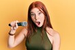 © Krakenimages.com - Young red head girl singing song using microphone scared and amazed with open mouth for surprise, disbelief face