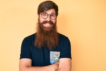 Wall Mural - Handsome young red head man with long beard wearing casual clothes and glasses happy face smiling with crossed arms looking at the camera. positive person.