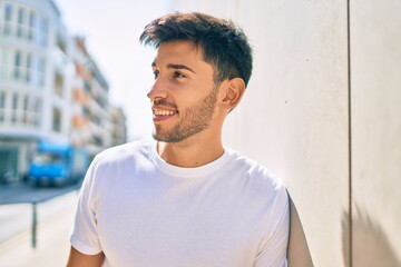 Young latin man smiling happy leaning on the wall at the city.