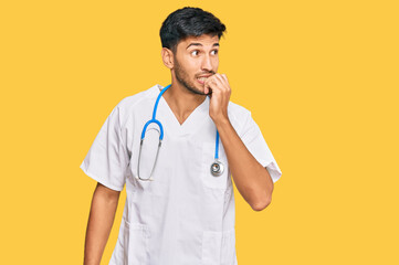 Young handsome man wearing doctor uniform and stethoscope looking stressed and nervous with hands on mouth biting nails. anxiety problem.