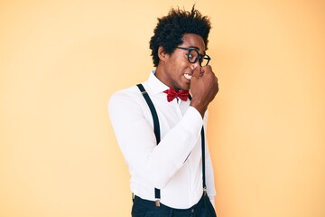 Poster - Handsome african american man with afro hair wearing hipster elegant look smelling something stinky and disgusting, intolerable smell, holding breath with fingers on nose. bad smell