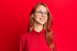 © Krakenimages.com - Young beautiful redhead woman wearing casual clothes and glasses over red background looking away to side with smile on face, natural expression. laughing confident.