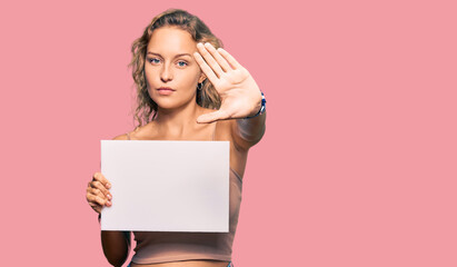 Wall Mural - Beautiful caucasian woman holding blank empty banner with open hand doing stop sign with serious and confident expression, defense gesture