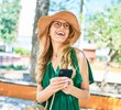 © Krakenimages.com - Young beautiful blonde woman on vacation wearing summer hat and glasses smiling happy. Standing with smile on face using smartphone at street of city.