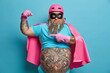 © wayhome.studio  - Serious bearded adult European man raises arm points at muscles dressed in superhero costume has thick beard isolated over blue studio background demonstrates his power. People strength concept