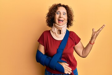 Poster - Beautiful middle age mature woman wearing cervical collar and arm on sling celebrating victory with happy smile and winner expression with raised hands