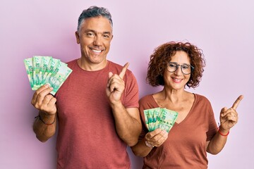 Sticker - Beautiful middle age couple holding south african 10 rand banknotes smiling happy pointing with hand and finger to the side