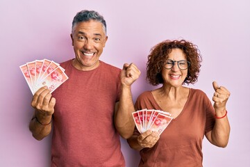 Sticker - Beautiful middle age couple holding 20 israel shekels banknotes screaming proud, celebrating victory and success very excited with raised arm