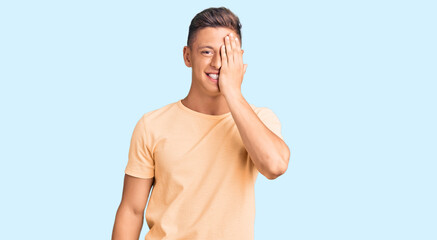 Sticker - Young handsome man wearing casual clothes covering one eye with hand, confident smile on face and surprise emotion.