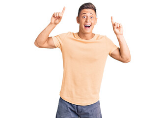 Wall Mural - Young handsome man wearing casual clothes smiling amazed and surprised and pointing up with fingers and raised arms.