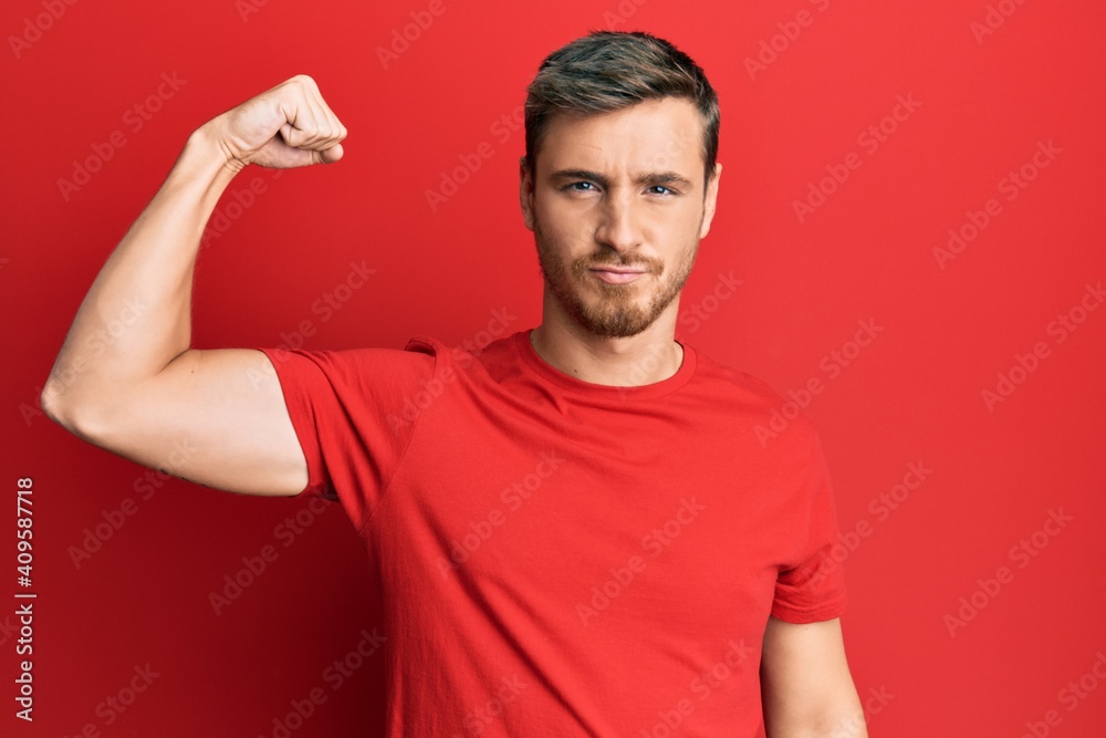 Handsome caucasian man wearing casual red tshirt strong person showing arm muscle, confident and proud of power - obrazy, fototapety, plakaty 