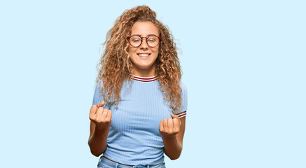 Poster - Beautiful caucasian teenager girl wearing casual clothes and glasses very happy and excited doing winner gesture with arms raised, smiling and screaming for success. celebration concept.