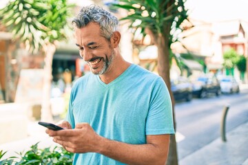 Poster - Middle age grey-haired man using smartphone at street of city looking positive and happy standing and smiling with a confident smile showing teeth