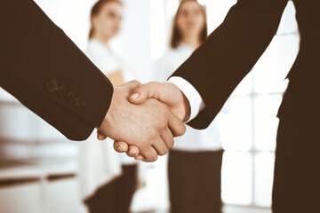 Businessman and woman shaking hands with colleagues at the background. Handshake at meeting in office. Concept of success in business