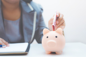 business woman putting coin in to piggy bank with calculate and note on paper account for accounting or financial and saving concept.