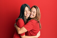 Hispanic Family Of Mother And Daughter Wearing Casual Clothes Over Red Background Hugging Oneself Happy And Positive, Smiling Confident. Self Love And Self Care