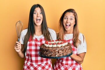 Poster - Hispanic family of mother and daughter wearing baker apron holding homemade cake celebrating crazy and amazed for success with open eyes screaming excited.