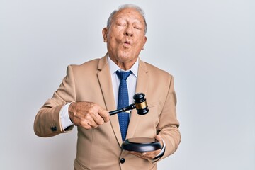 Canvas Print - Senior caucasian judge man using gavel making fish face with mouth and squinting eyes, crazy and comical.