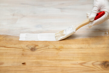 A hand in a protective glove with a brush paints a wooden surface