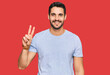 © Krakenimages.com - Young hispanic man wearing casual clothes smiling looking to the camera showing fingers doing victory sign. number two.