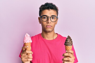 Wall Mural - Young handsome african american man holding ice cream cones relaxed with serious expression on face. simple and natural looking at the camera.