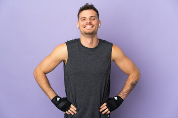 Wall Mural - young caucasian handsome man isolated on purple background posing with arms at hip and smiling