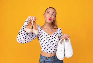 Pensive woman holding pair of high heels shoes and sneakers