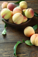 Wall Mural - Fresh harvest of peaches in a clay bowl on a wooden rustic table. Peach leaves are present in the composition.