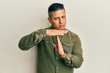 Young latin man wearing casual clothes doing time out gesture with hands, frustrated and serious face