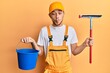 Hispanic young man wearing glass cleaner uniform and squeegee making fish face with mouth and squinting eyes, crazy and comical.