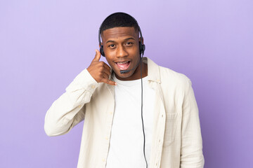 Telemarketer latin man working with a headset isolated on purple background making phone gesture. Call me back sign