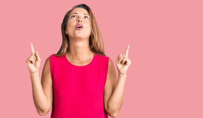 Poster - Middle age hispanic woman wearing casual clothes amazed and surprised looking up and pointing with fingers and raised arms.