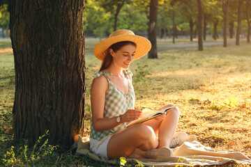 Young woman reading book on green grass near tree in park