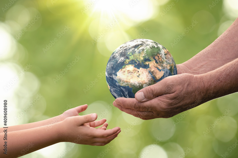 Close up of senior hands giving small planet earth to a child over defocused green background with copy space - obrazy, fototapety, plakaty 