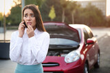 Fototapeta  - Stressed woman talking on phone near broken car outdoors