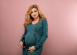 © rubchikova - Portrait of a pregnant woman in a green dress on a pink background