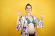 © Irene - Young beautiful woman pregnant expecting baby wearing pajama over isolated yellow background showing and pointing up with fingers number six while smiling confident and happy