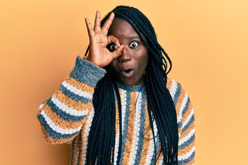 Sticker - Young black woman with braids wearing casual winter sweater doing ok gesture shocked with surprised face, eye looking through fingers. unbelieving expression.