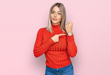 Beautiful blonde woman wearing casual clothes in hurry pointing to watch time, impatience, looking at the camera with relaxed expression